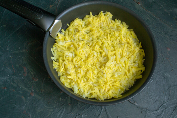 Spread the potato mixture evenly in the pan to form a large, thin pancake. Spreading the grated potato mixture in a hot skillet with oil to form a large pancake.