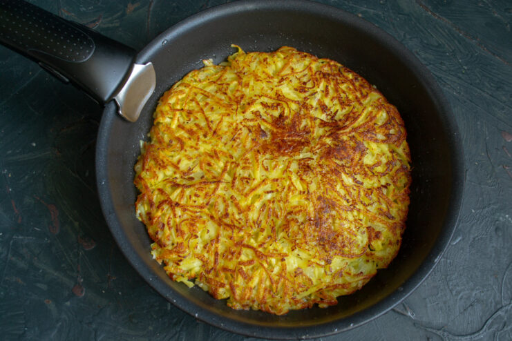 Slide the pancake back into the skillet to cook the other side. Sliding the partially cooked potato pancake from a plate back into the skillet.