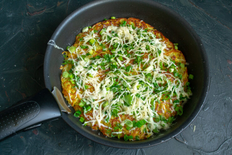 Adding cheese and herbs on top while the second side cooks allows the cheese to melt perfectly. Sprinkling chopped herbs and grated cheese over the potato pancake in the skillet.