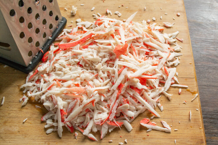 How to Prepare Crab Sticks for Patties Frozen crab sticks being grated on a coarse box grater into a bowl.
