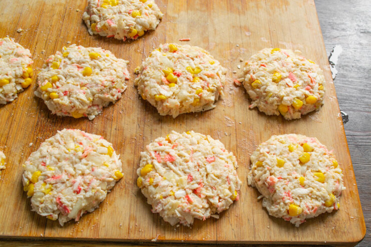 Shaping the Crab Stick Patties Perfectly formed round, uncooked crab stick patties arranged on a wooden cutting board.