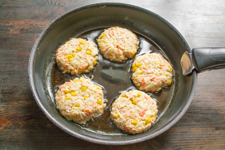 Frying the Crab Stick Patties Placing uncooked crab stick patties into a hot frying pan with oil using a spatula.