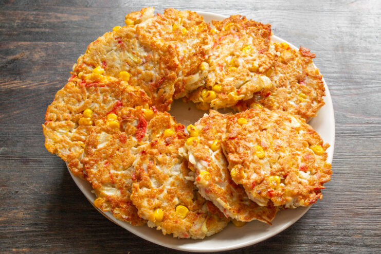 Serving Suggestion for Crab Stick Patties A plate of freshly cooked crab stick patties served with a side of sauce and garnished with chopped green onions.