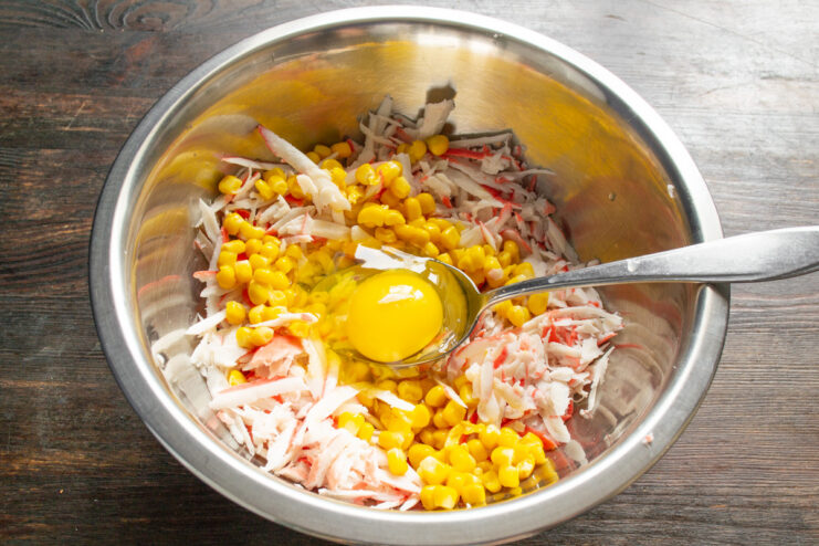 Adding Eggs to the Crab Stick Mixture Two eggs cracked into the bowl with grated crab sticks and corn.