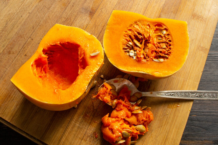 How to prepare butternut squash for soup: scooping out the seeds. A hand scooping seeds out of a halved butternut squash with a spoon.