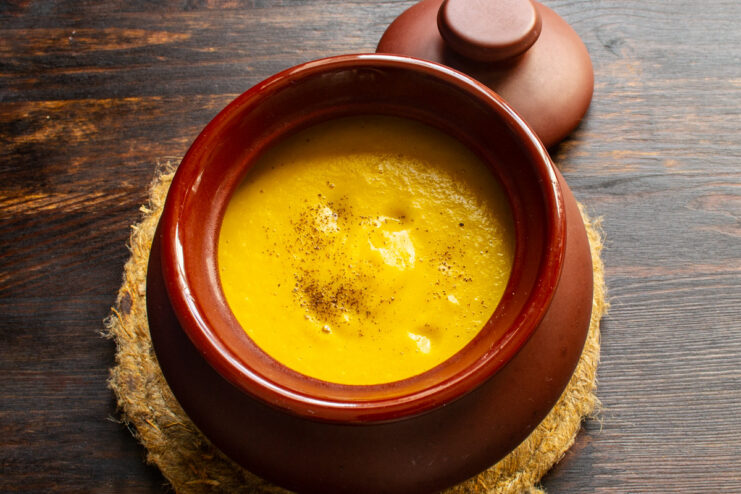Serving the finished soup, garnished with pepper and nutmeg. Creamy pumpkin and lentil soup being ladled into a white bowl for serving.