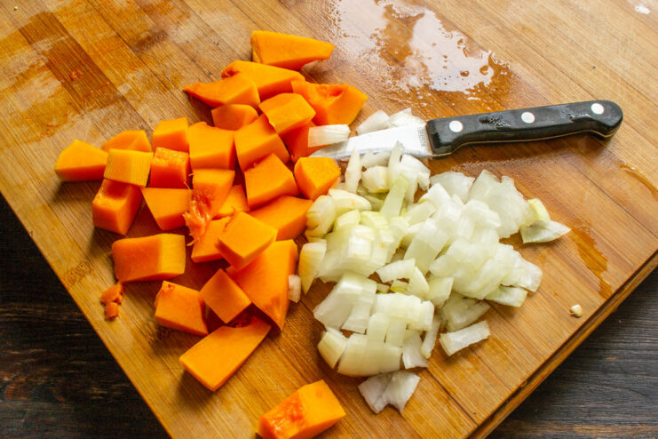 Dicing butternut squash into uniform cubes for even cooking. Peeled and diced butternut squash on a cutting board.