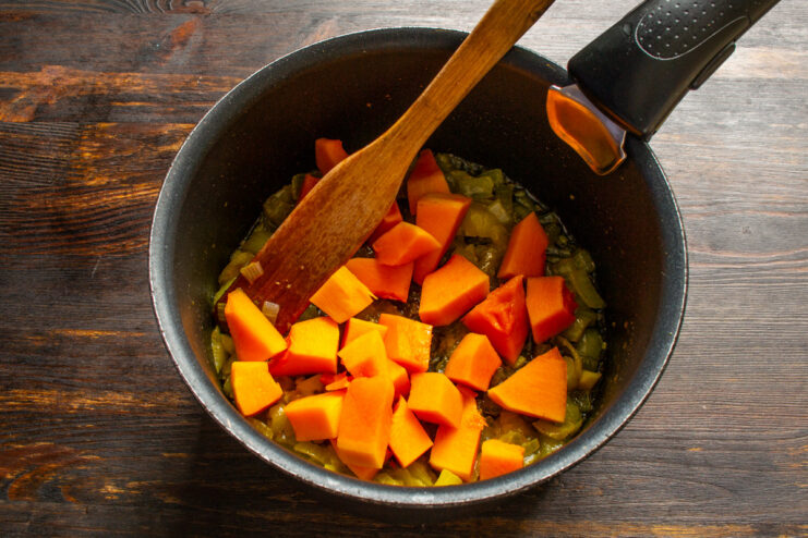 Adding freshly grated nutmeg to the pumpkin for a warm, aromatic flavor. Grating fresh nutmeg over diced pumpkin in a pan.