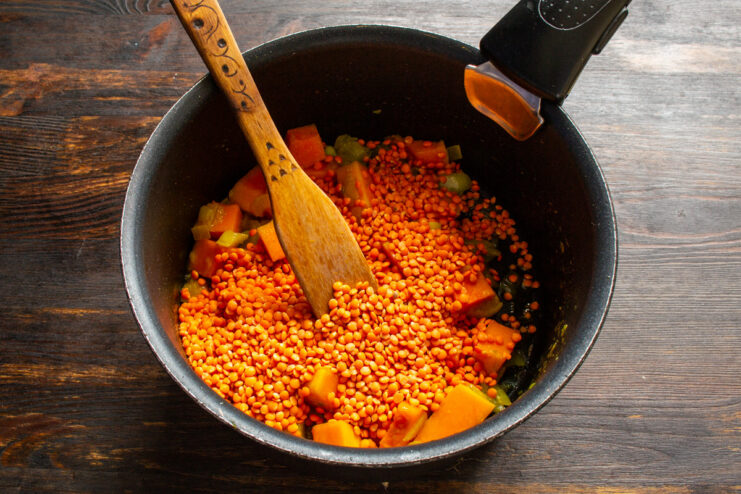 Adding red lentils to the soup pot. They cook quickly and add creaminess. Red lentils being added to the pan with sautéed pumpkin and onion.