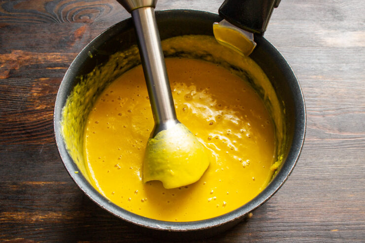 Using an immersion blender to create a perfectly smooth and creamy soup. An immersion blender pureeing the pumpkin and lentil soup directly in the pot.
