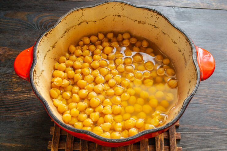 A glass bowl filled with dry chickpeas soaking in clear water.