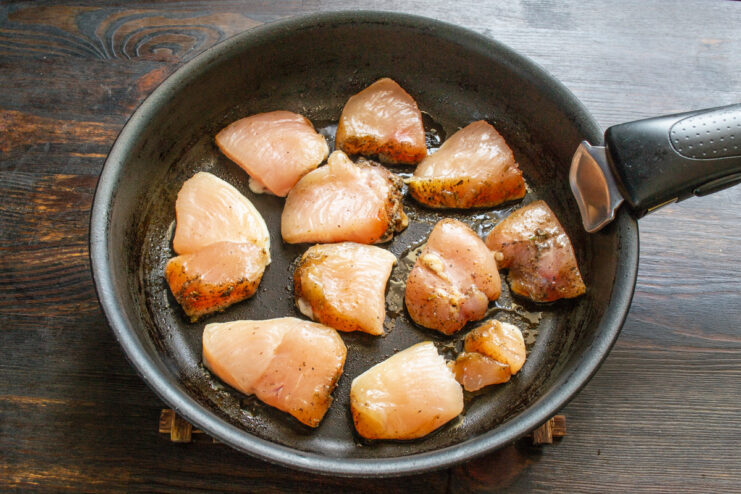 Sliced chicken breast pieces being placed onto a hot non-stick skillet.