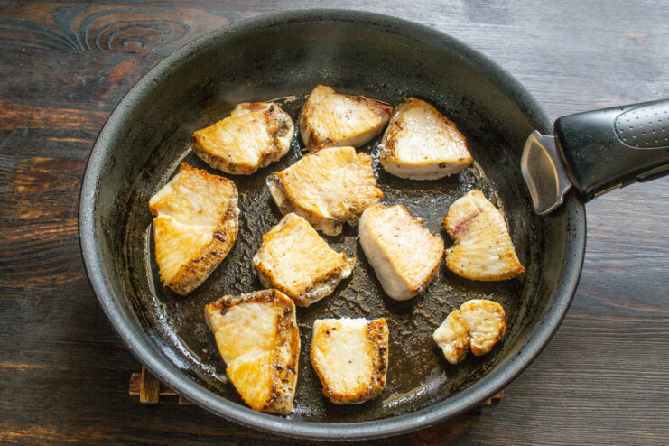Golden-brown chicken pieces sizzling in a black skillet.