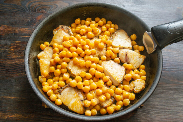 Cooked chickpeas being added to the skillet with the fried chicken.