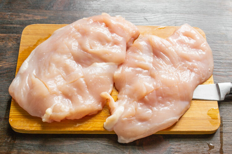 Preparing the Chicken Fillets for Frying Two raw chicken breast fillets on a cutting board being prepared for cooking.
