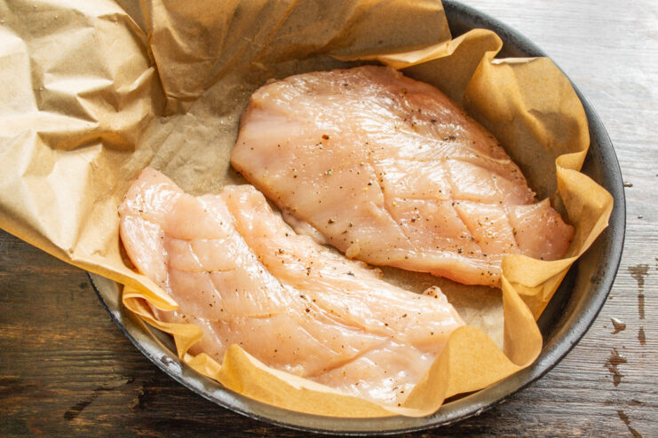 Cooking Chicken on Parchment Paper in a Pan Seasoned chicken breast placed on parchment paper inside a frying pan.