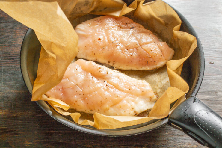 Searing the Chicken Breast on One Side Chicken breast searing on one side in a pan lined with parchment paper.