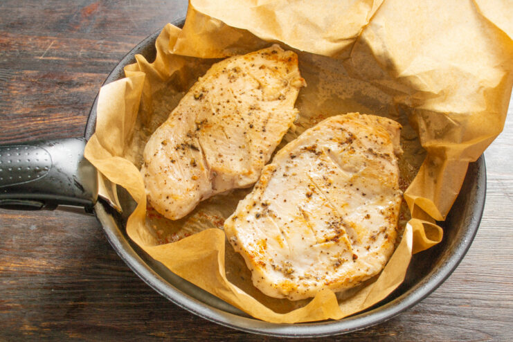 Tip: Cover with Parchment to Speed Up Cooking Parchment paper being folded over the chicken breast in the pan to trap heat.