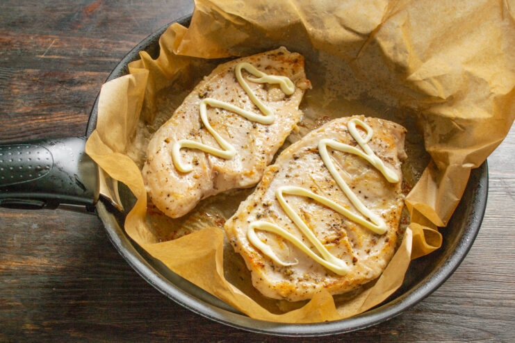 Adding a Touch of Mayonnaise for Flavor A spoonful of mayonnaise being spread on the cooked chicken breast.