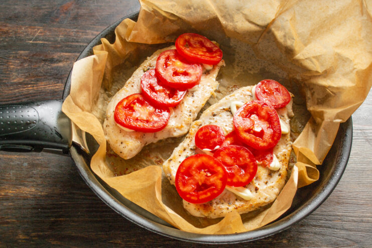 Layering Fresh Tomato Slices on the Chicken Thin slices of fresh tomato being placed on top of the chicken breast in the pan.