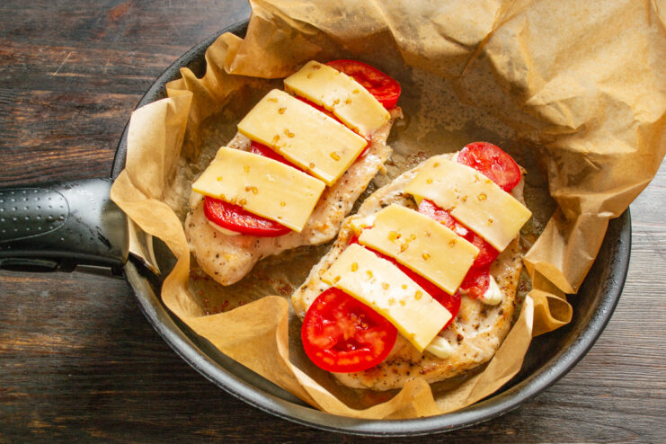 Topping with Cheese Before Melting Slices of cheese being placed over the tomatoes on the chicken breast.