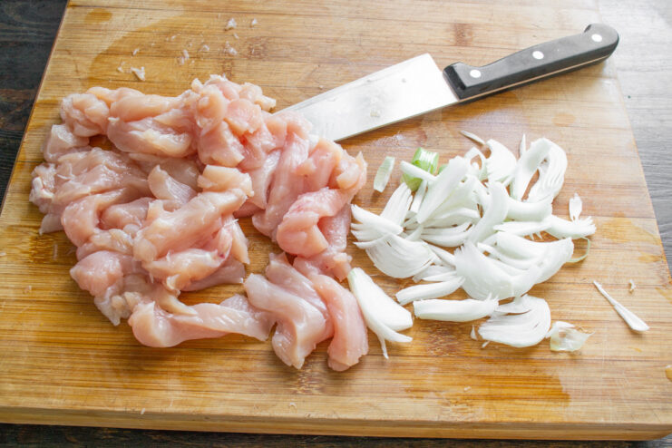 How to Properly Slice Chicken Breast for Stir-Frying Raw chicken breast being sliced into thin strips on a cutting board.
