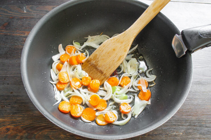 Adding Carrots to the Stir-Fry Thinly sliced carrots being added to the wok with sautéed onions.