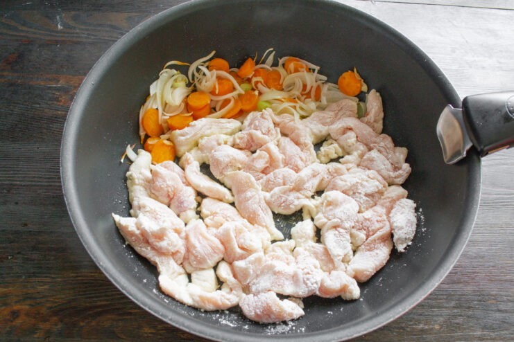Cooking Chicken and Vegetables in the Same Pan Vegetables pushed to one side of the wok, with starch-coated chicken pieces being added to the other side.