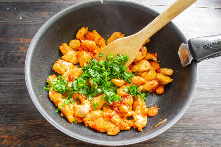 Finishing the Dish with Fresh Cilantro Finely chopped fresh cilantro being added to the chicken and vegetable stir-fry in a wok.