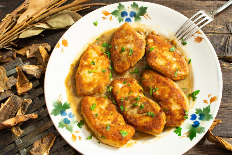A plate of golden-brown chicken fillet covered in a creamy mushroom sauce, garnished with parsley.