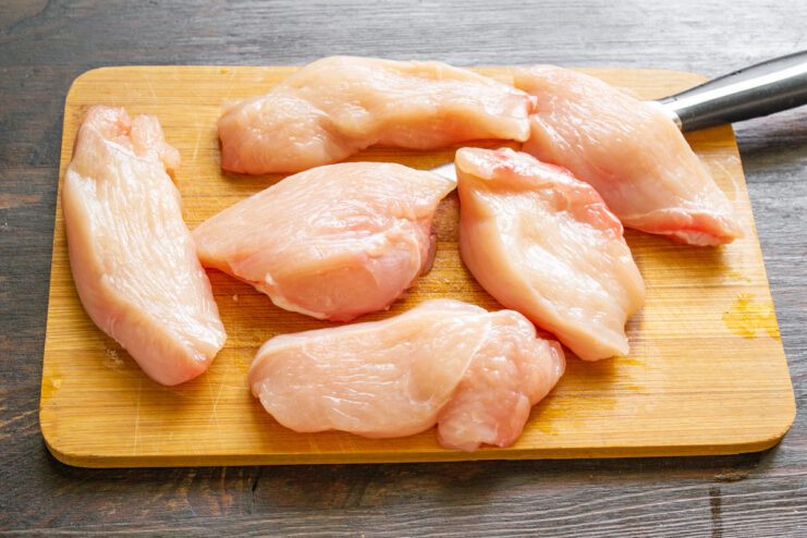 Slicing Chicken Breast into Medallions for Frying Raw chicken breast being sliced into thick medallions on a cutting board.