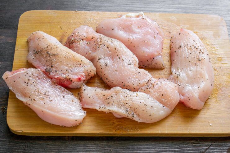 Seasoning Chicken Fillets Before Marinating Seasoned chicken medallions on a cutting board, covered with plastic wrap.