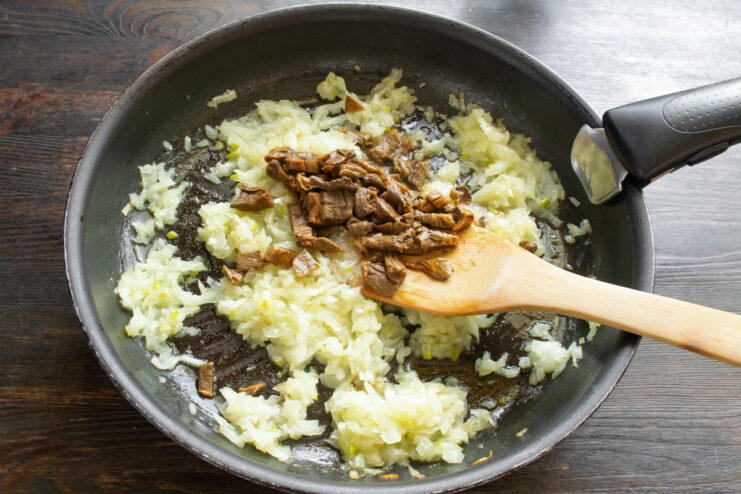 Adding Chopped Mushrooms to Sautéed Onions Finely chopped boiled mushrooms being added to a pan with sautéed onions.