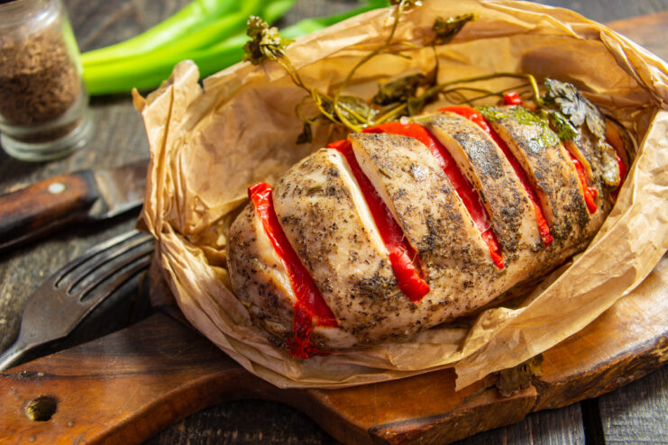 A plate with cooked chicken fillet baked in a parchment envelope, garnished with herbs.