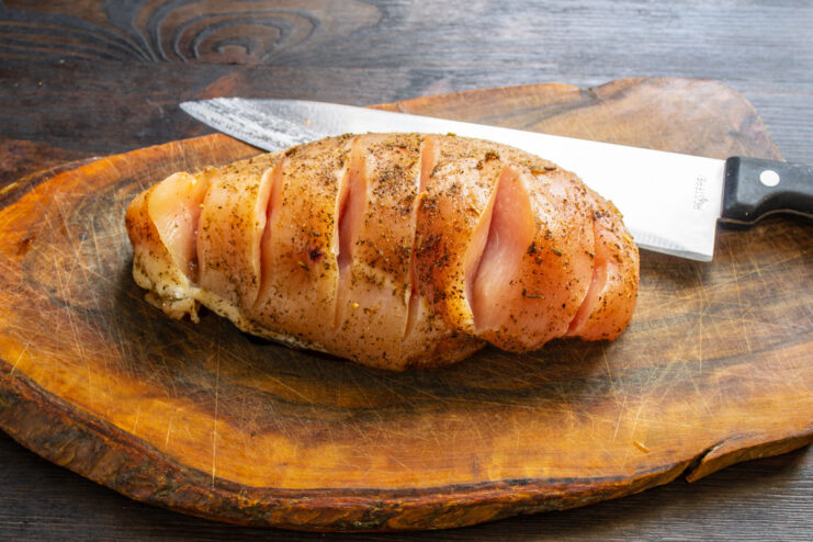 How to Prepare Chicken for Stuffing - Making Incisions A hand using a sharp knife to make several parallel cuts into a marinated chicken fillet.
