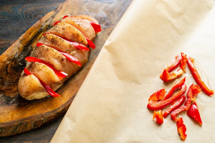 Creating a Vegetable Bed for the Chicken on Parchment Paper A bed of sliced red bell pepper on a sheet of parchment paper.