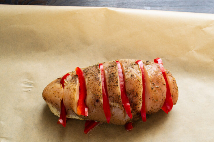 Assembling the Chicken en Papillote - Placing Chicken on Peppers The stuffed chicken fillet placed on top of a bed of sliced peppers on parchment paper.