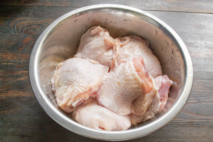 Step 1: Preparing the Chicken Thighs for Marinating Raw chicken thighs in a white bowl being rinsed with water in a sink.