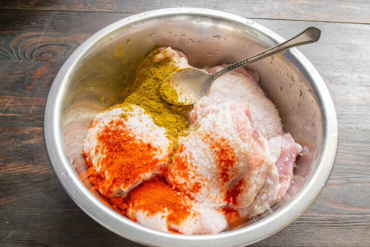 Step 2: Seasoning the Chicken for Maximum Flavor Seasoning being sprinkled over raw chicken thighs in a bowl.