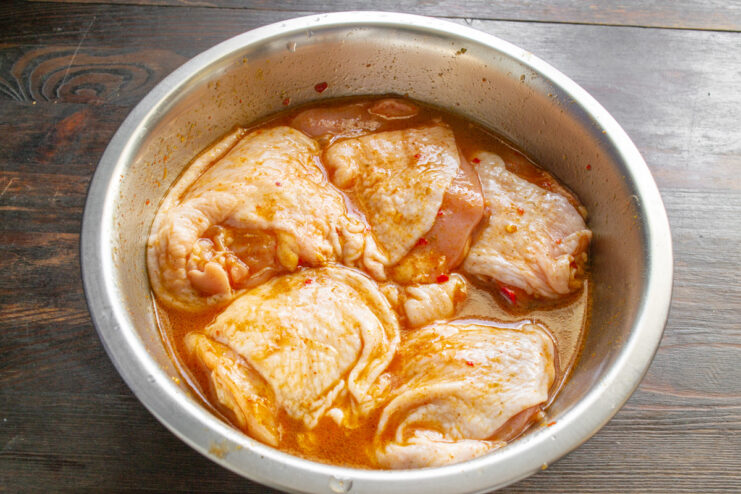 Step 4: Letting the Chicken Marinate to Absorb Flavors A bowl of chicken thighs marinating, covered with plastic wrap.