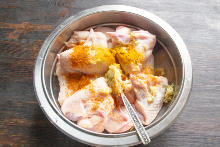 Adding Spices for a Flavorful Marinade Spices, including red paprika and yellow turmeric, being added to a bowl of raw chicken wings.