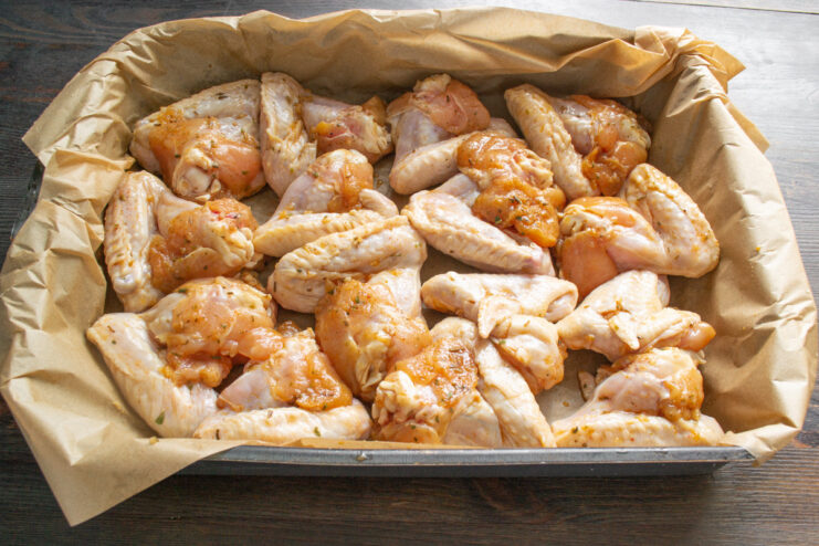 Arranging Wings on a Baking Sheet for Even Cooking Marinated chicken wings arranged in a single layer on a parchment-lined baking sheet.