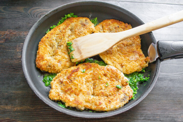 Coating the Schnitzels in Cilantro Butter Sauce Fried chicken schnitzels being coated with a fragrant cilantro and butter sauce in a skillet.