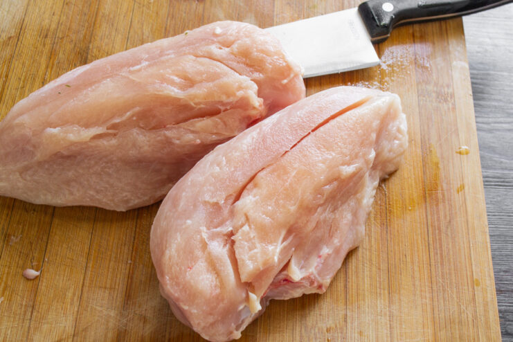 Preparing the Chicken: Separating the Tenderloin from the Breast Fillet A hand holding a knife is separating the chicken tenderloin from the main breast fillet on a cutting board.