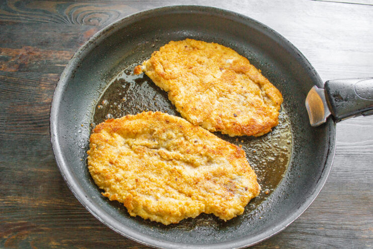 Frying Chicken Schnitzels to a Golden Brown Two chicken schnitzels frying in a pan, turning a beautiful golden-brown color.