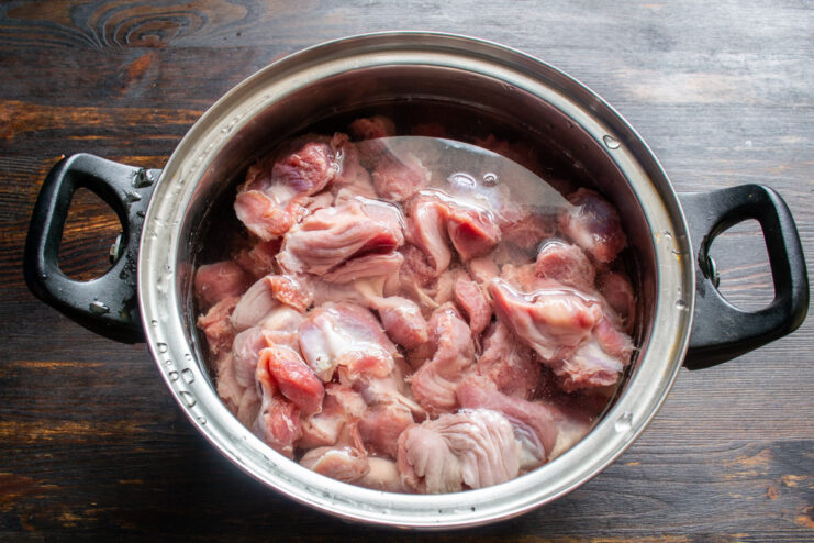 Step 1: Parboiling the chicken gizzards to ensure tenderness. Raw chicken gizzards in a stainless steel pot being covered with water.