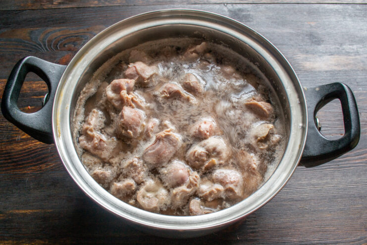 Rinsing the parboiled gizzards before stewing. Boiled chicken gizzards being rinsed in a metal colander under running water.