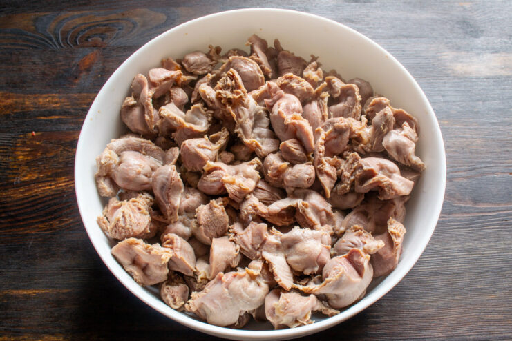 Arranging the parboiled gizzards in the baking dish. Parboiled chicken gizzards layered in a clear glass baking dish.