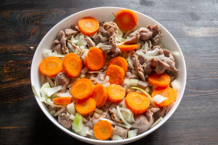 Adding sliced carrots for sweetness and color. Round carrot slices being added to the baking dish with gizzards and onions.