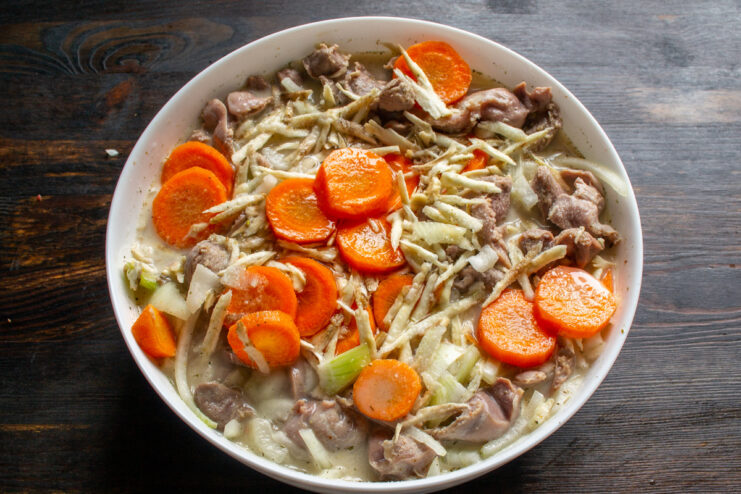 Covering the gizzards and vegetables with the creamy sauce. Pouring the prepared white smetana sauce over the gizzards and vegetables.